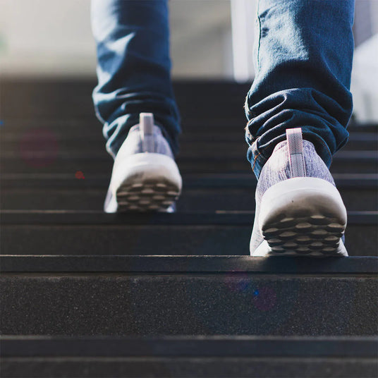 A person wearing blue jeans and white sneakers walking up a dark outdoor staircase.