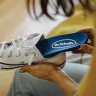 Image of person putting a Dr. Scholl's padded shoe insert in tennis shoe.