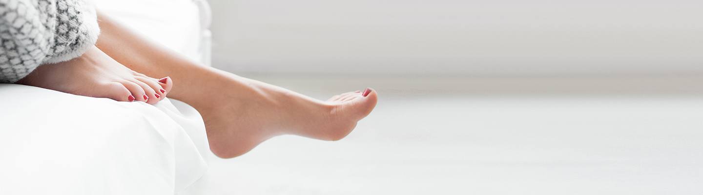 Image of a woman's feet hanging over the  side of a bed. 
