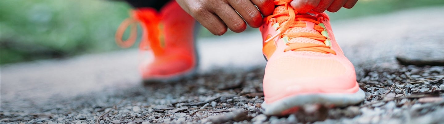 Image of a person leaned over tying  jogging shoes. 